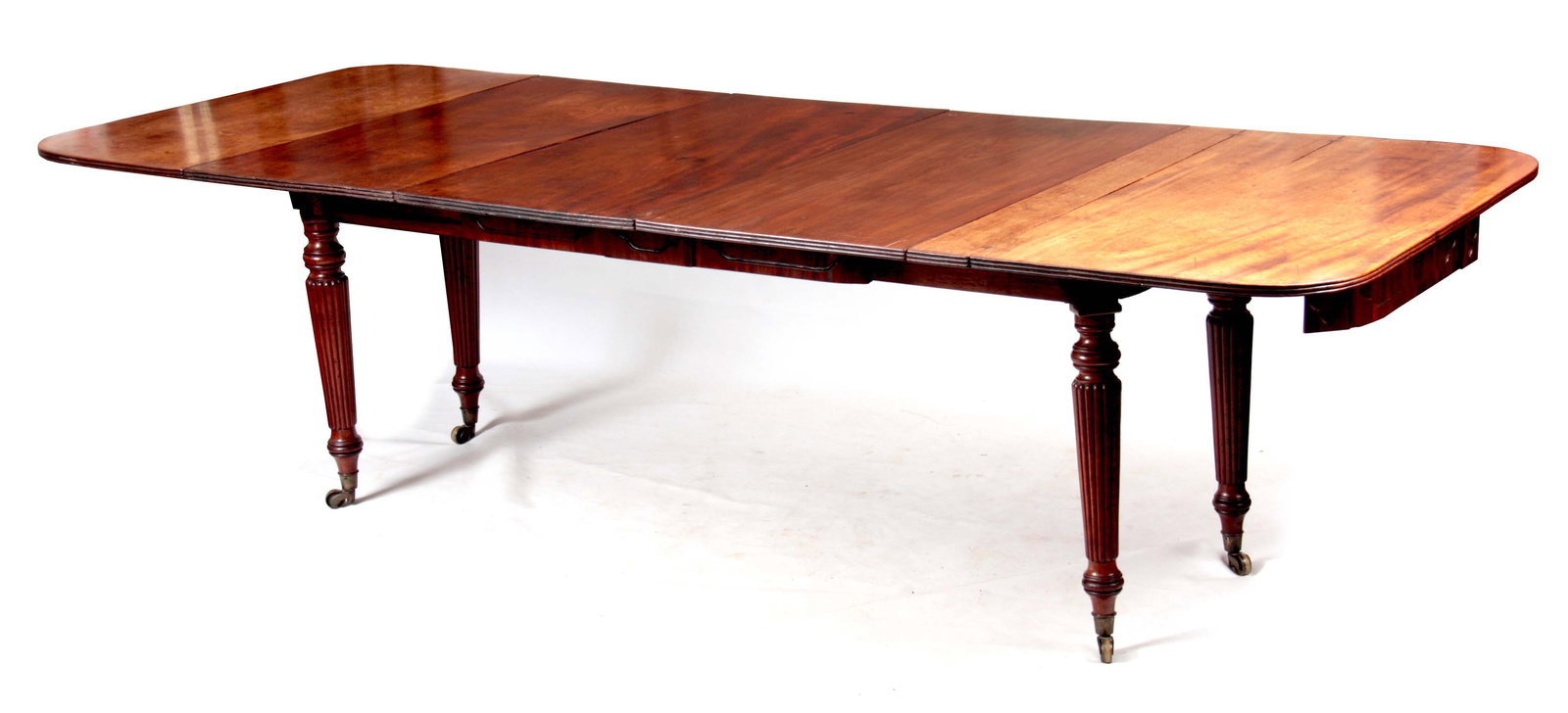 A FINE REGENCY ENGLISH MAHOGANY EXTENDING DINING TABLE WITH STEWART PATENT MECHANISM IN THE MANNER: A FINE REGENCY ENGLISH MAHOGANY EXTENDING DINING TABLE WITH STEWART PATENT MECHANISM IN THE MANNER OF GILLOWS the rounded rectangular top with three removable leaves above a Gothic panelled frieze, th