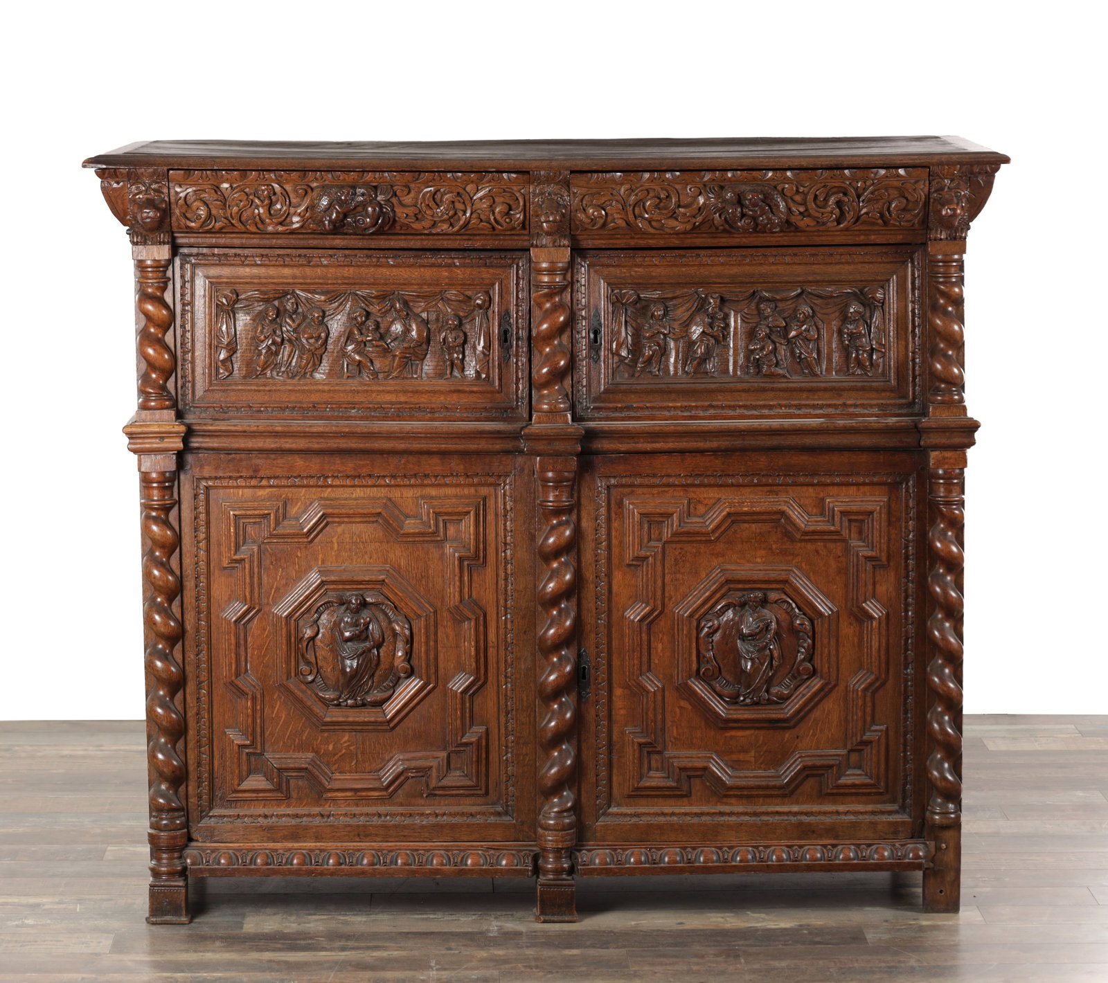 A 17TH CENTURY EUROPEAN CARVED OAK CUPBOARD IN TWO PARTS WITH BARLEY TWIST PILASTERS: A 17TH CENTURY EUROPEAN CARVED OAK CUPBOARD IN TWO PARTS WITH BARLEY TWIST PILASTERS the oversailing top above a frieze carved with foliate scrolls and masks incorporating two short drawers, above a p