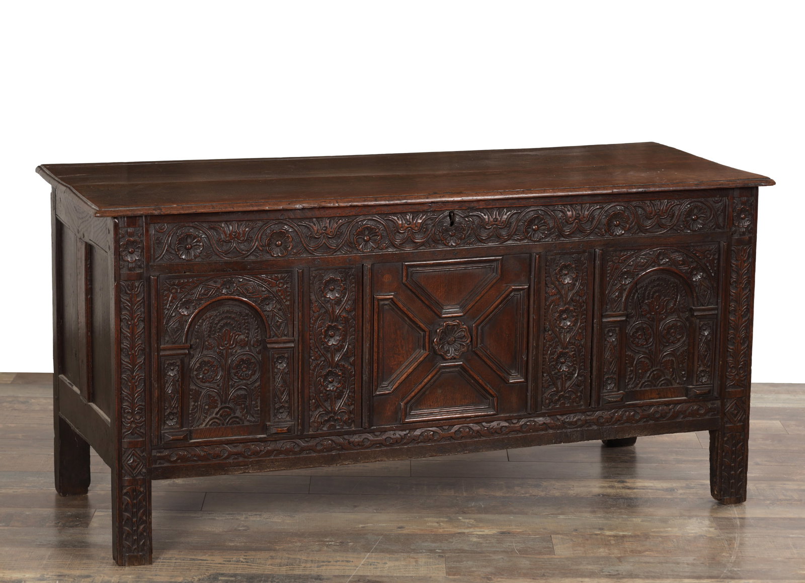A 17TH CENTURY ENGLISH OAK CARVED COFFER: A 17TH CENTURY ENGLISH OAK CARVED COFFER with a hinged plank top above a foliate carved frieze and a three-panel front, the central panel with a raised geometric lozenge and rosette boss flanked by ar