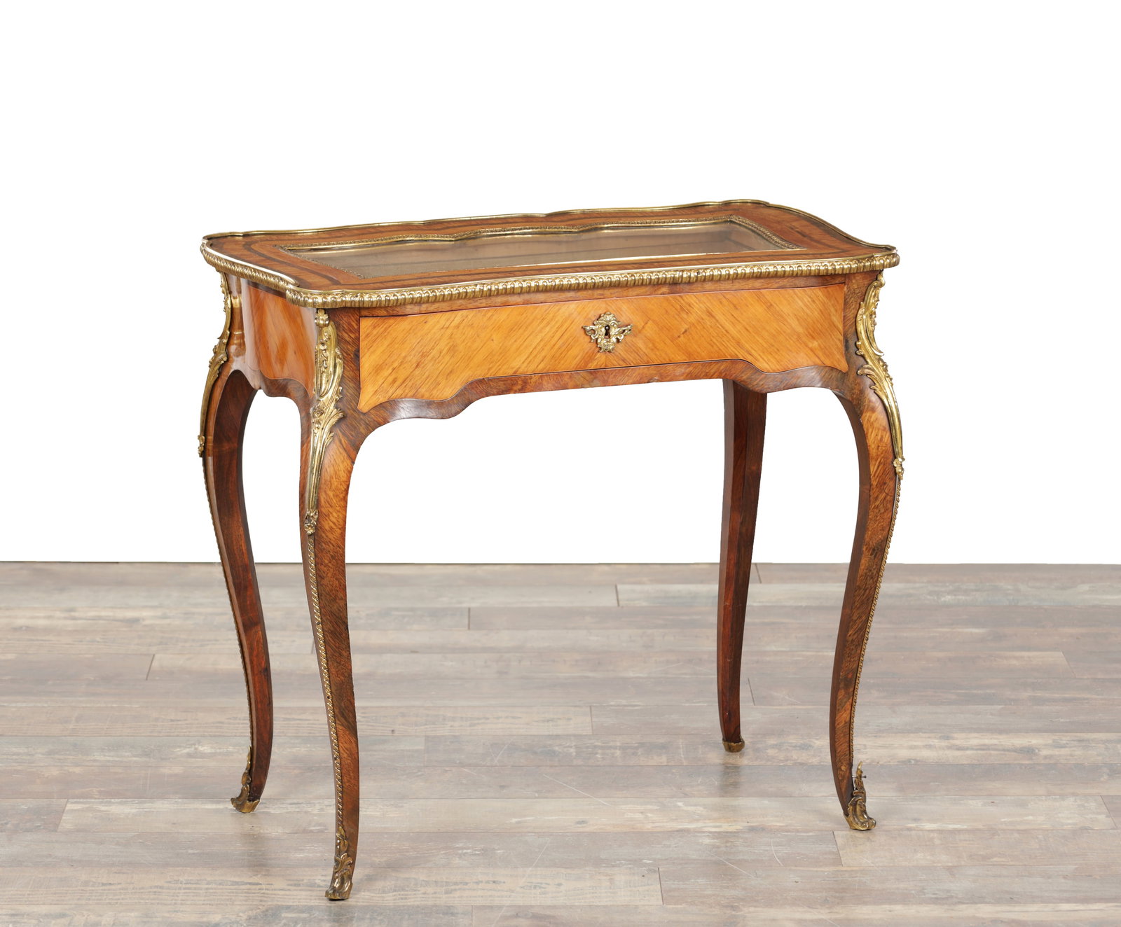 A 19TH CENTURY ROSEWOOD AND KINGWOOD ORMOLU MOUNTED BIJOUTERIE TABLE: A 19TH CENTURY ROSEWOOD AND KINGWOOD ORMOLU MOUNTED BIJOUTERIE TABLE of serpentine outline with a glazed top within a beaded ormolu border and shaped frieze centred by an escutcheon, the kingwood vene