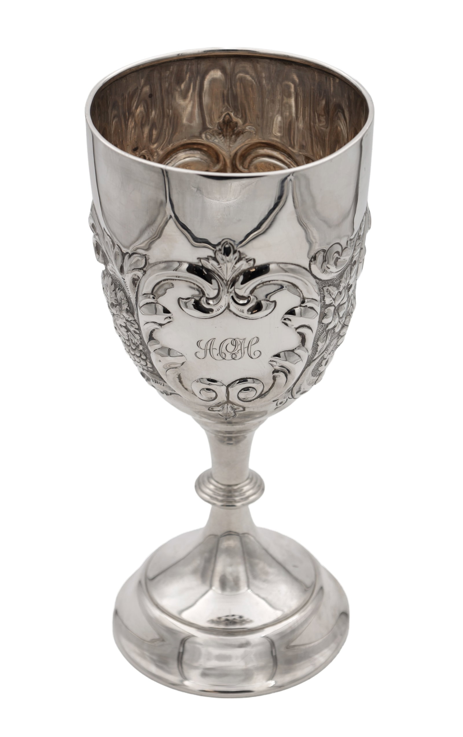 A SILVER TROPHY CUP WITH REPOUSSE DECORATION: A SILVER TROPHY CUP WITH REPOUSSE DECORATION of goblet form with shaped scroll cartouche engraved with a monogram and foliate panels, raised on a knopped stem and stepped circular foot. (28cm high,)