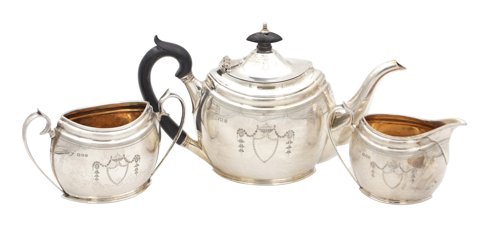 A GEORGE V ENGLISH SILVER THREE PIECE TEA SET: A GEORGE V ENGLISH SILVER THREE PIECE TEA SET of oval baluster form with bright-cut swag and shield cartouche decoration, comprising teapot, sugar bowl and cream jug, the teapot with ebonised handle