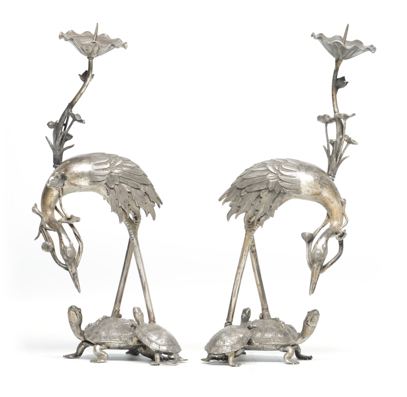 A PAIR OF MEIJI PERIOD JAPANESE WHITE METAL CANDLESTICKS FORMED AS CRANES STANDING ON TORTOISES: A PAIR OF MEIJI PERIOD JAPANESE WHITE METAL CANDLESTICKS FORMED AS CRANES STANDING ON TORTOISES each with a lotus stem rising behind to a petalled sconce, the cranes with downturned heads clasping