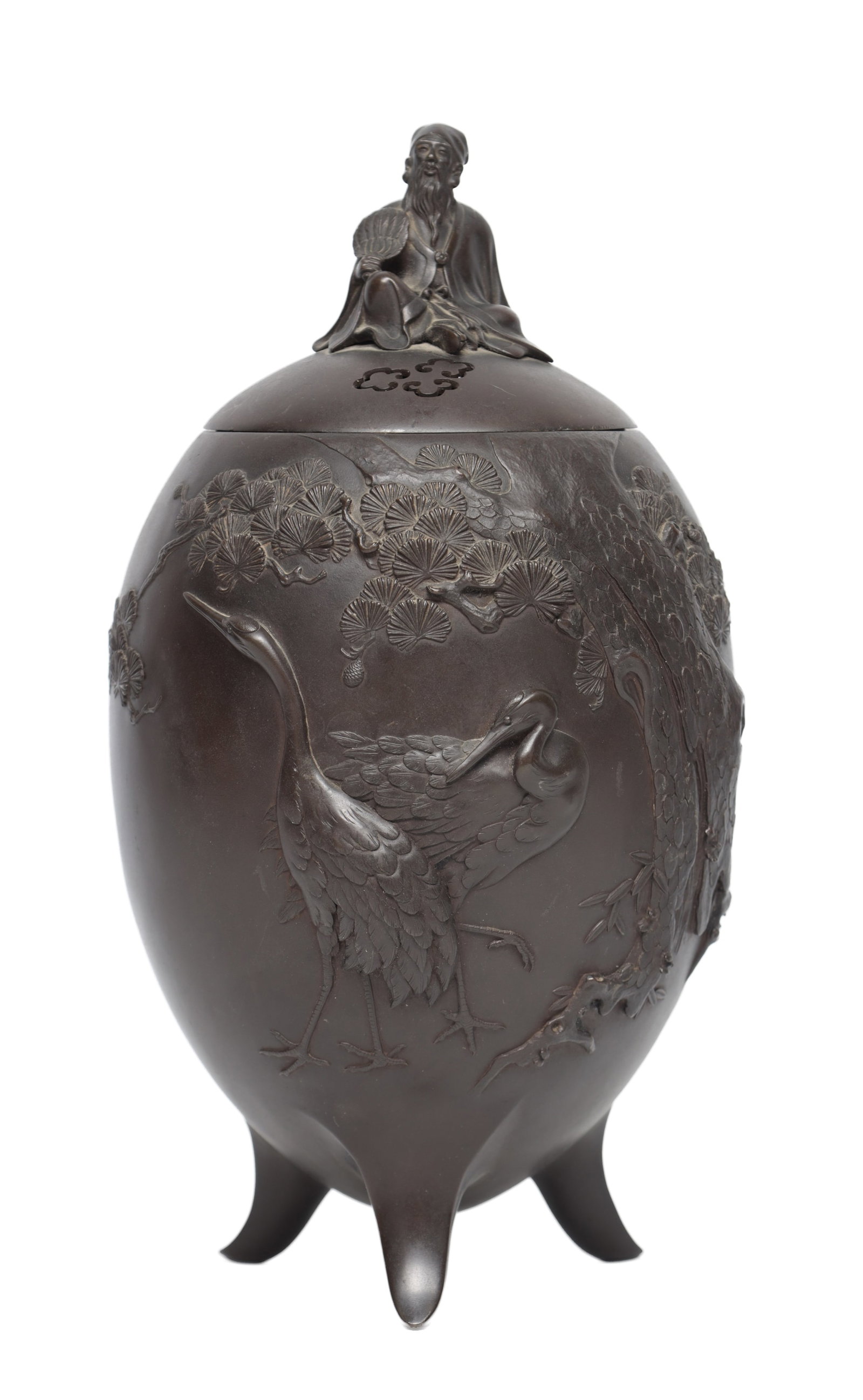 A JAPANESE MEIJI PERIOD BRONZE LIDDED VASE: A JAPANESE MEIJI PERIOD BRONZE LIDDED VASE of ovoid tripod form with a domed cover surmounted by a seated sage holding a fan, the body in high relief with cranes beneath pine, the cover with pierced