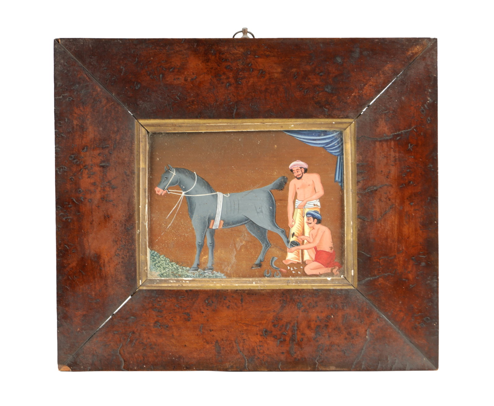 A LATE 18TH/EARLY 19TH CENTURY INDIAN REVERSE GLASS PAINTING: A LATE 18TH/EARLY 19TH CENTURY INDIAN REVERSE GLASS PAINTING depicting two grooms shoeing a grey horse before a brown ground with a blue curtain, in a burr wood frame with gilt slip. (13cm high,