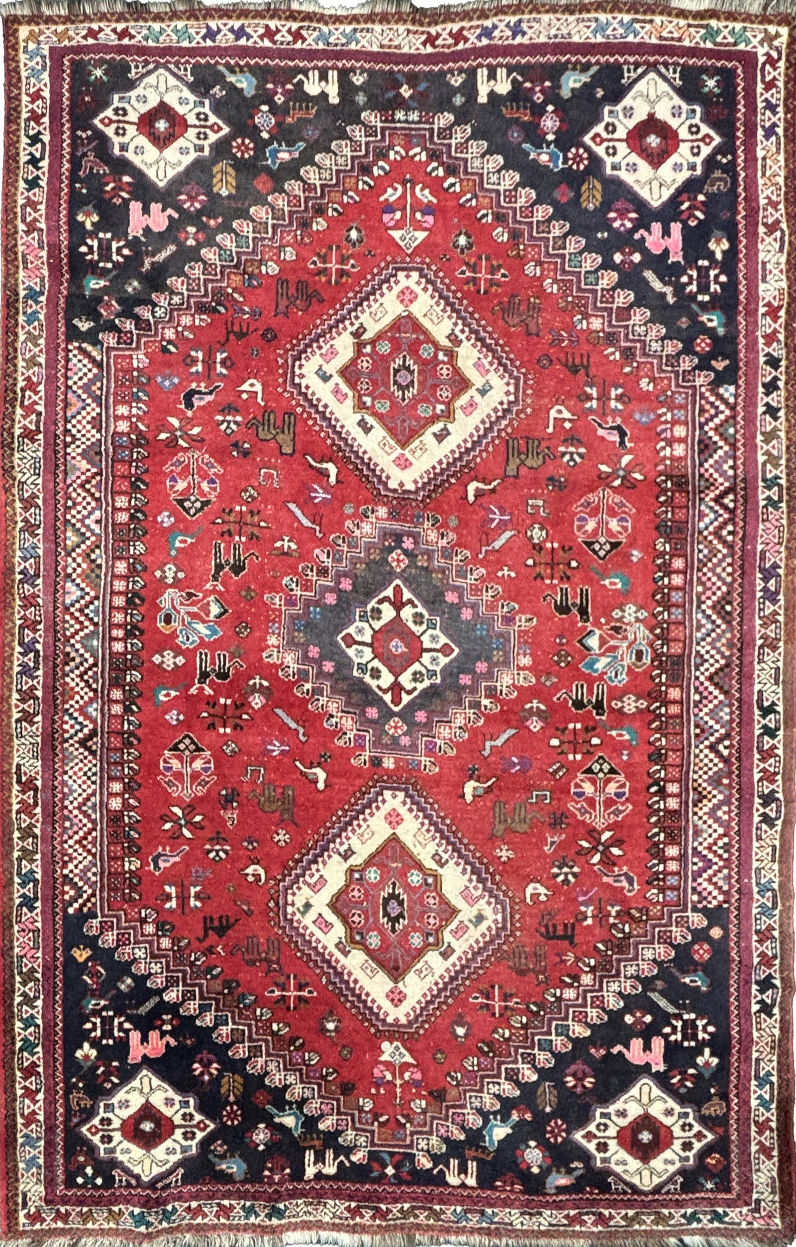 A LARGE ANTIQUE PERSIAN WOOL CARPET: A LARGE ANTIQUE PERSIAN WOOL CARPET with triple diamond medallions on a madder red ground with dark blue spandrels, scattered stylised animals and boteh motifs within multiple geometric borders.
