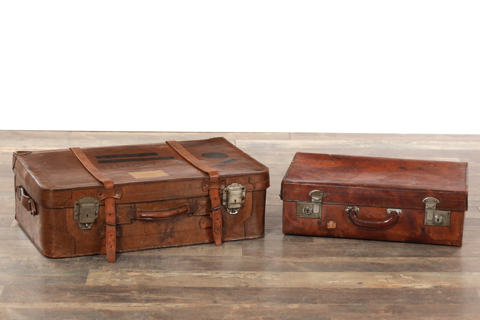 TWO VINTAGE LEATHER SUITCASES: TWO VINTAGE LEATHER SUITCASES comprising a larger and a smaller example, each of rectangular form with stitched leather exteriors, fitted leather carrying handles and metal clasp locks, the interiors