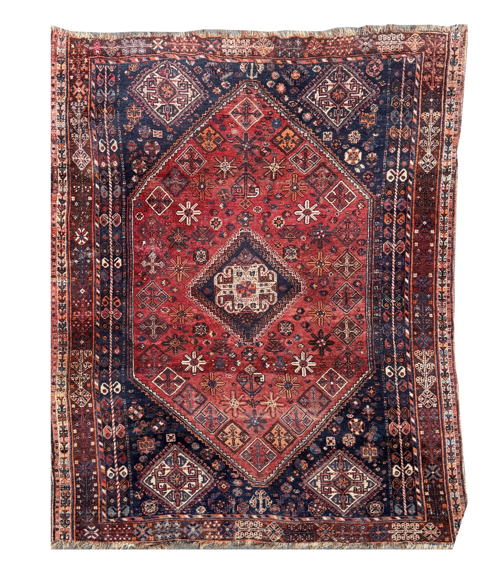 A PERSIAN SHIRAZ HAND-KNOTTED WOOL CARPET: A PERSIAN SHIRAZ HAND-KNOTTED WOOL CARPET with a central stepped diamond medallion on a madder red field scattered with stylised rosettes and geometric devices, indigo spandrels and multiple guarded b