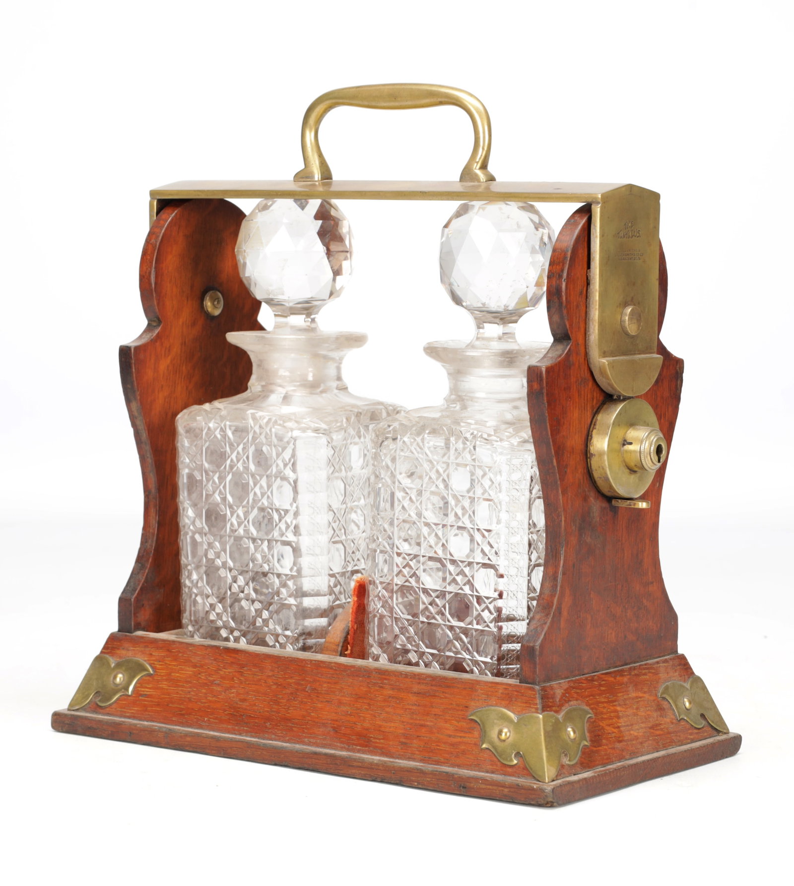 A LATE 19TH CENTURY ENGLISH OAK AND BRASS TANTALUS WITH TWO CUT GLASS DECANTERS: A LATE 19TH CENTURY ENGLISH OAK AND BRASS TANTALUS WITH TWO CUT GLASS DECANTERS of open frame form with brass carry handle and locking mechanism, the square decanters with diamond and cross-cut decora