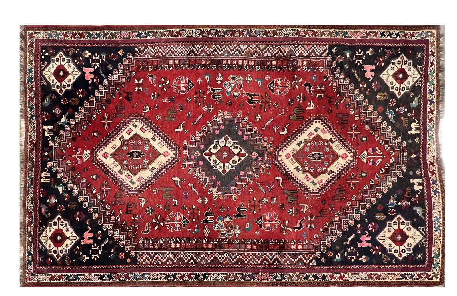A PERSIAN WOOL CARPET WITH TRIPLE MEDALLION AND ANIMAL MOTIFS: A PERSIAN WOOL CARPET WITH TRIPLE MEDALLION AND ANIMAL MOTIFS with three serrated lozenge medallions on a red ground scattered with stylised birds, animals and rosettes, indigo spandrels to the