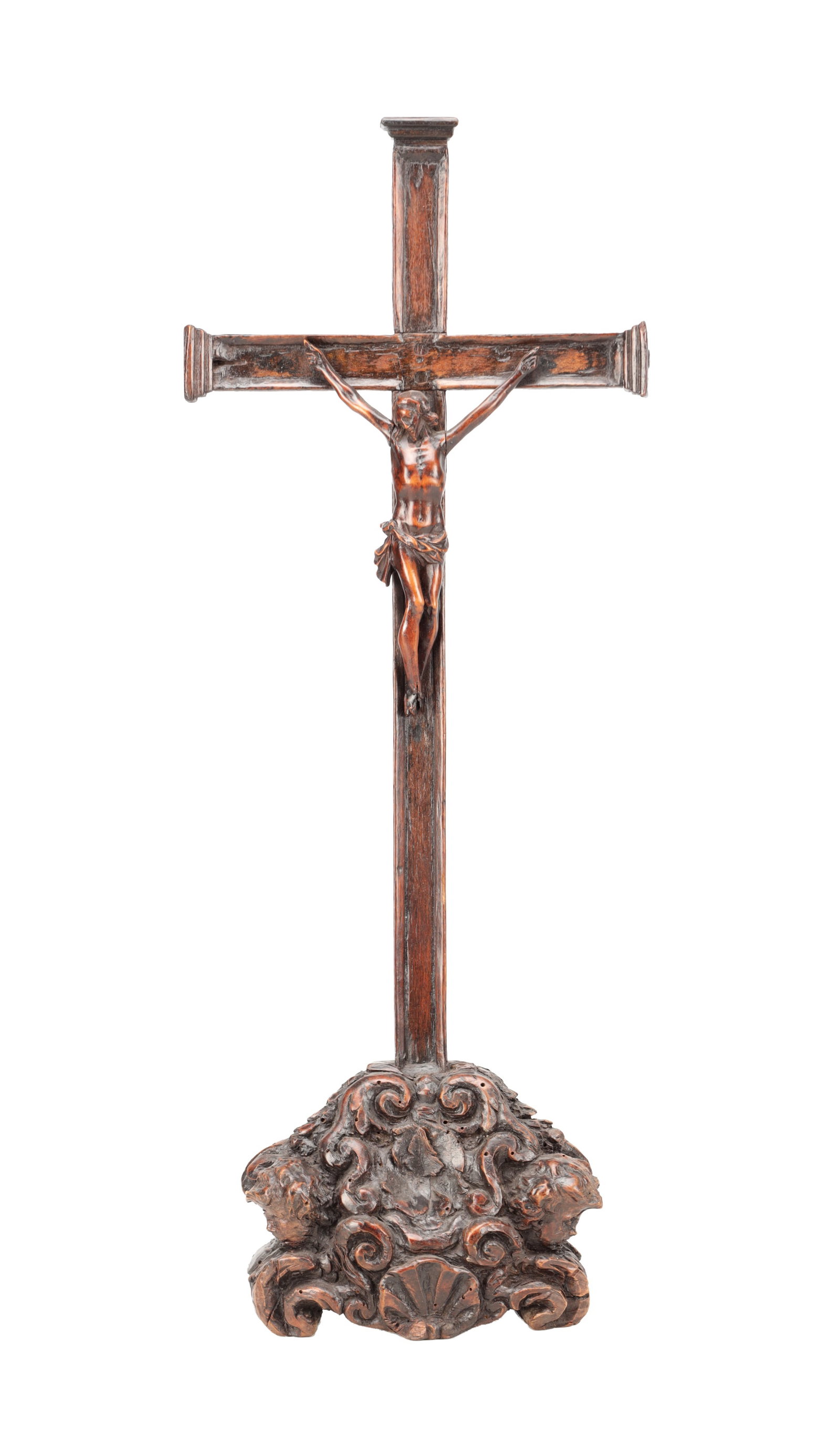 A 17TH CENTURY CARVED WALNUT CRUCIFIX ON A BAROQUE SCROLL BASE: A 17TH CENTURY CARVED WALNUT CRUCIFIX ON A BAROQUE SCROLL BASE with a naturalistically modelled Corpus wearing a perizoma on a rectangular cross with moulded terminals, raised on a shaped plinth carve