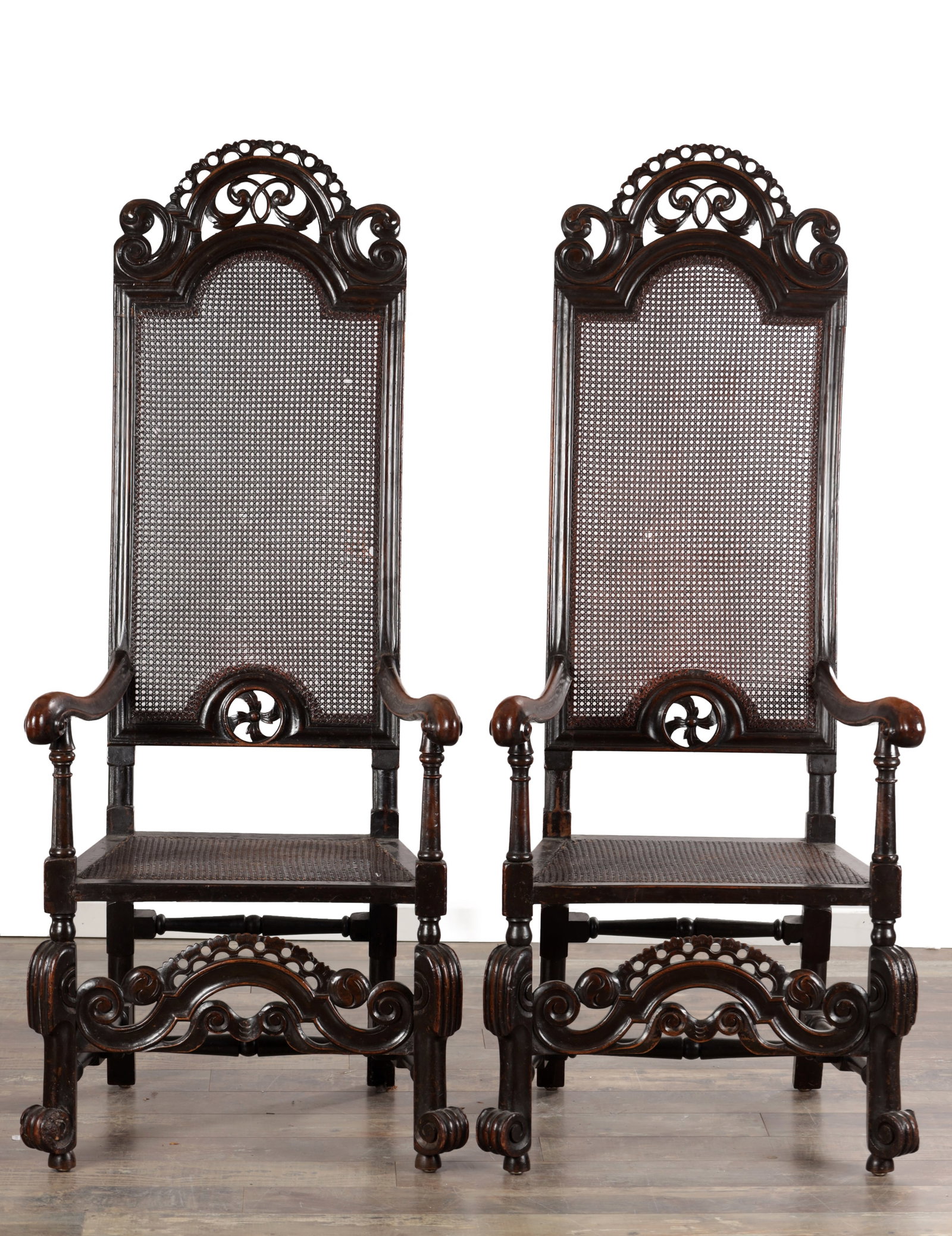 A PAIR OF WILLIAM AND MARY WALNUT HIGH-BACK CANED ARMCHAIRS: A PAIR OF WILLIAM AND MARY WALNUT HIGH-BACK CANED ARMCHAIRS with arched and pierced scroll crestings above cane panel backs and seats, outswept scrolled arms on turned uprights, raised on block and ba