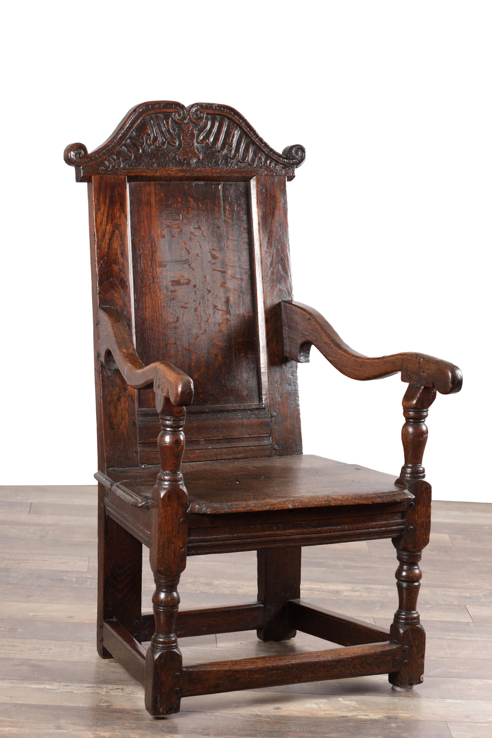 A 17TH CENTURY YORKSHIRE OAK WAINSCOT ARMCHAIR: A 17TH CENTURY YORKSHIRE OAK WAINSCOT ARMCHAIR with a scrolled and foliate carved cresting above a panelled back, shaped open arms on ring-turned supports and a boarded seat with moulded rails,