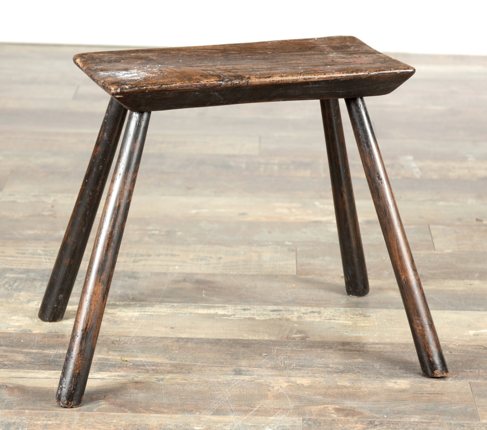 A 19TH CENTURY OAK CHEESE TOP STOOL: A 19TH CENTURY OAK CHEESE TOP STOOL with a rectangular chamfered seat and gently dished top raised on four splayed round legs. (39cm high, 50cm wide, 35cm deep)