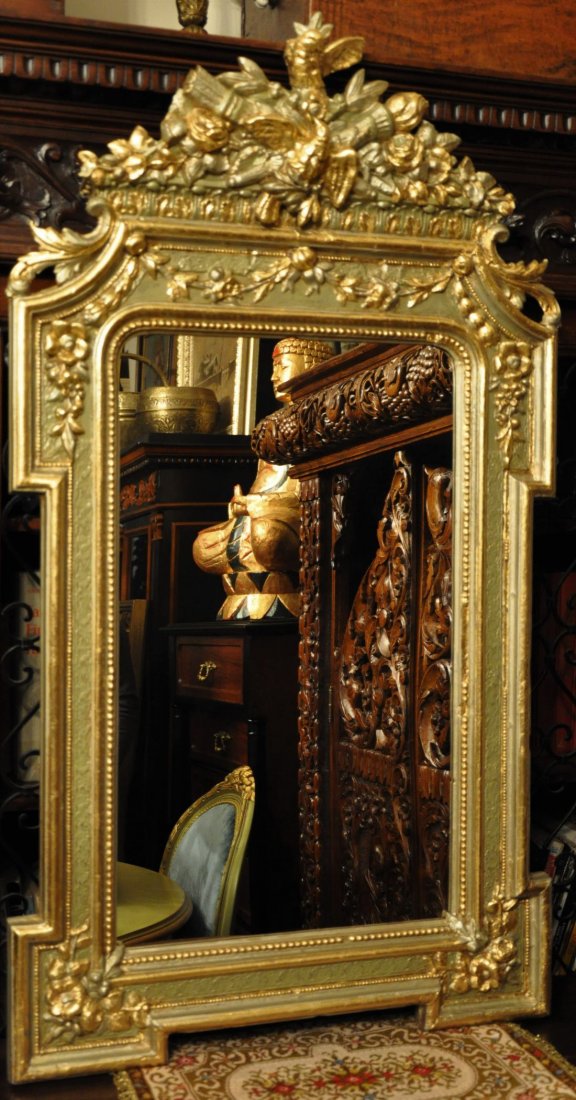 Hand carved wooden mirror with golden decorations: Hand carved wooden mirror with gilded birds and flower decorations on a light green painted surface.