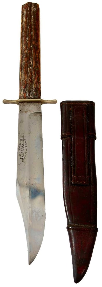 A SMALL BOWIE KNIFE BY JOHN CLARKE & SON,: 15cm clipped back blade stamped JOHN CLARKE & SON SHEFFIELD N.E.V.A. CORPORATE MARK, shaped nickel crossguard, two-piece riveted natural stag?s horn grips in its leather sheath. Clean blade with p