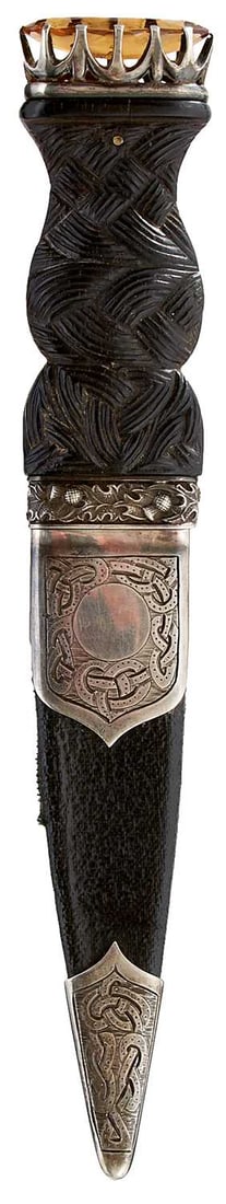 A SCOTTISH SILVER MOUNTED SGIAN DUBH,: 8cm fullered blade with partially faceted back edge, wooden grip (some splits) carved with Celtic knotwork to the front and with entwined thistle collar, amber coloured stone pommel, leather wrapped