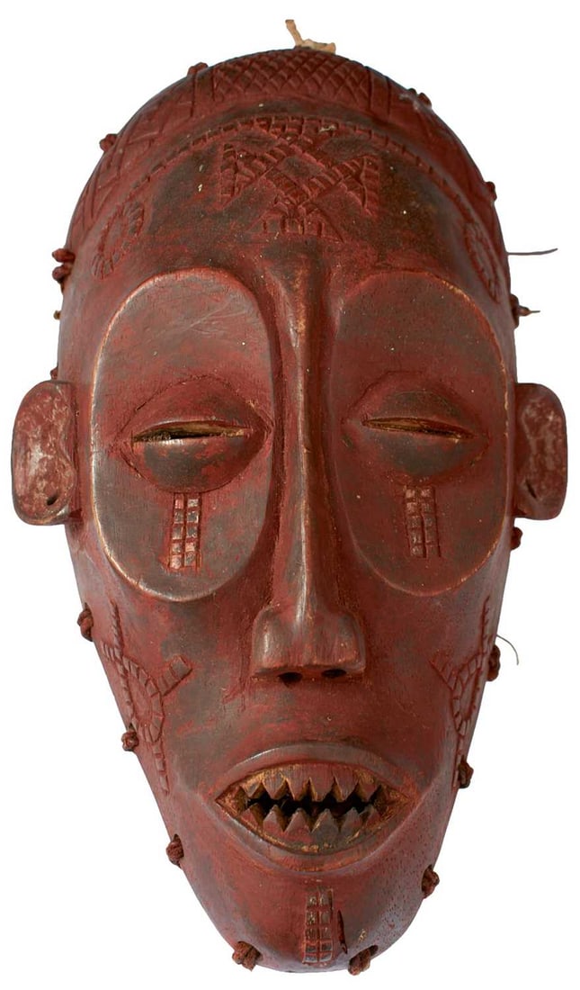 TRIBAL ART - AN ANGOLAN CHOKWE MASK,: the red painted carved wooden mask with string net hood to the reverse, together with a Cameroonian Bamum dance mask and a Himalayan mask. All late 19th Century or early 20th Century. (3)