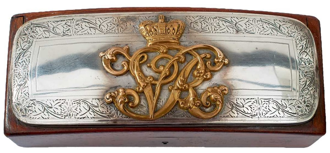 A VICTORIAN OFFICER'S SHOULDER BELT POUCH FLAP,: the white metal pouch cover with foliate engraved border and central pierced brass crowned VR cypher, now mounted as a desk tidy on a mahogany box with burgundy velvet lining.