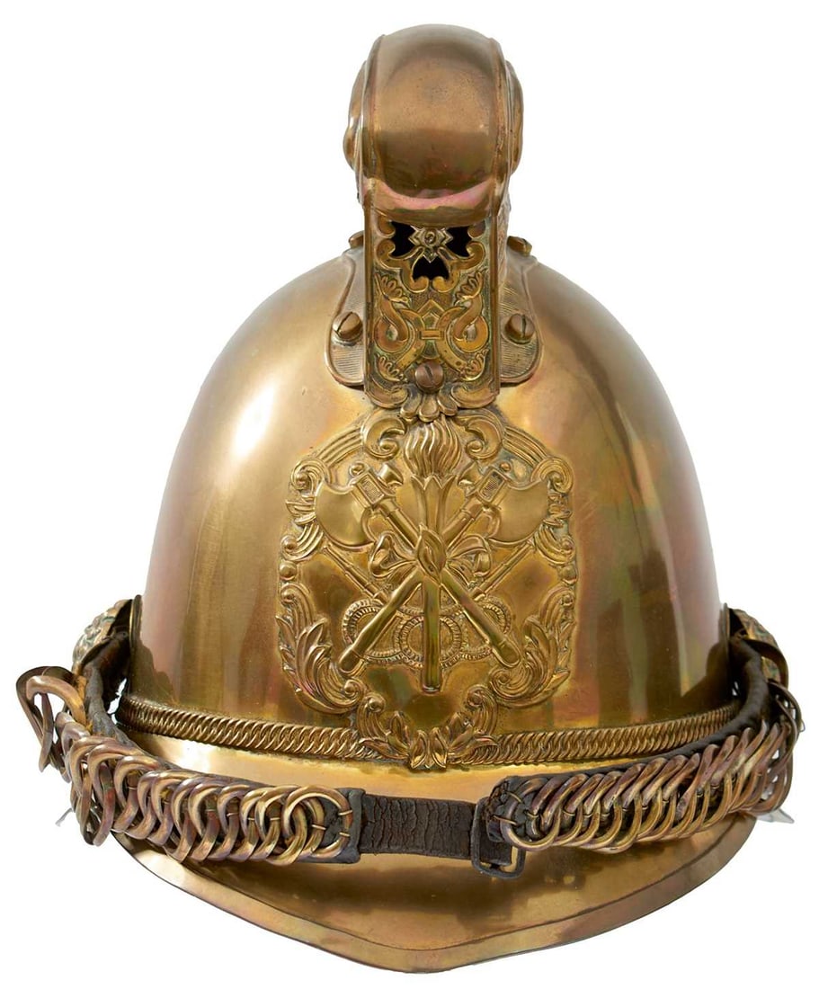 A BRASS FIREMAN'S HELMET,: the brass skull with embossed rococo helmet plate decorated with crossed axes motif, raised comb embossed with a winged dragon, pierced to the front with a vent, rosette bosses, leather backed chin ch