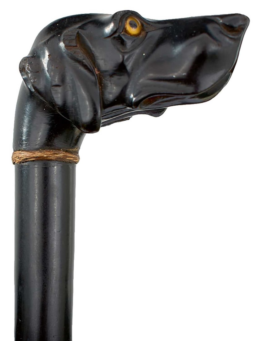 TWO DOG'S HEAD WALKING STICKS,: one carved ebonised wood, the handle depicting a hound with yellow glass eyes, briar haft, lacking ferrule, 90cm long over all, the other primitively carved as an elongated dog's head with glass eyes