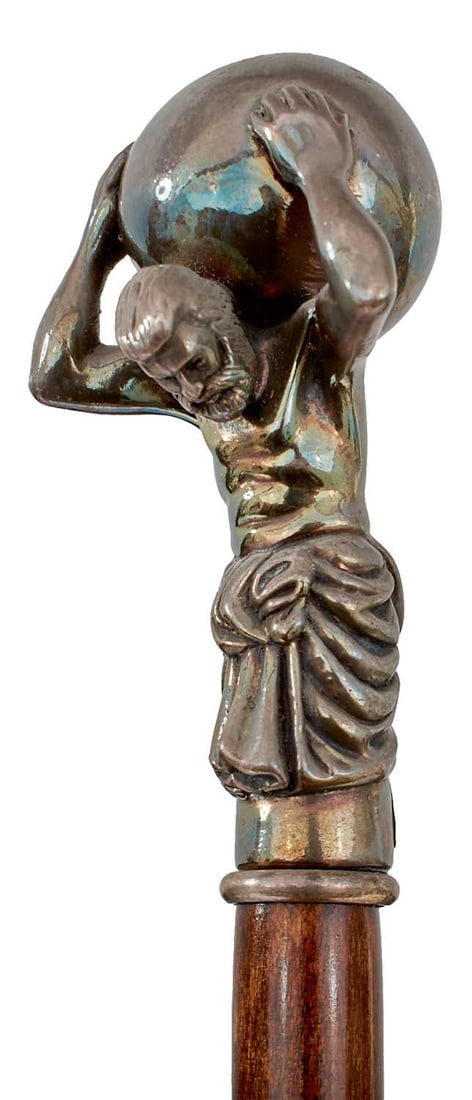 AN EARLY 20TH CENTURY WALKING STICK OF CLASSICAL GREEK INTEREST,: the white metal handle formed as Atlas bearing the world on his shoulders, tapering wooden haft, metal ferrule, 96cm long over all.