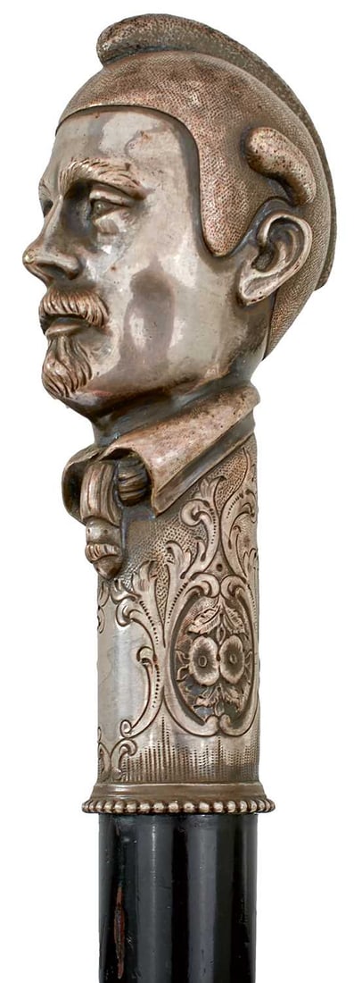 AN EARLY 20TH CENTURY WALKING STICK,: the pewter handle cast as the head of a gentleman on scrolling foliate collar, tapering wooden haft, metal ferrule, 89cm long over all.