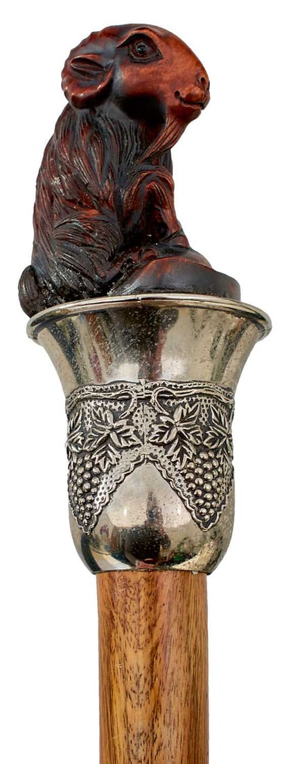 AN EARLY 20TH CENTURY WALKING STICK,: the handle with carved wood handle in the form of a goat seated on a white metal plinth decorated with fruiting grapevines, tapering wooden haft with silver collar inscribed IN TOKEN OF FAITHFUL