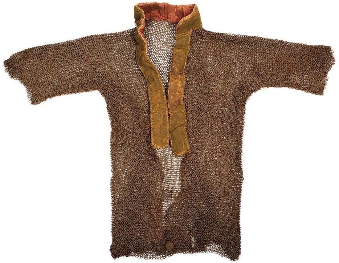 A 17TH CENTURY INDIAN SIKH MAIL SHIRT,: A 17TH CENTURY INDIAN SIKH MAIL SHIRT, the thigh length short sleeved shirt with padded collar, some repairs to cloth, composed of alternate rows of riveted and solid rings, circular brass armoury tag