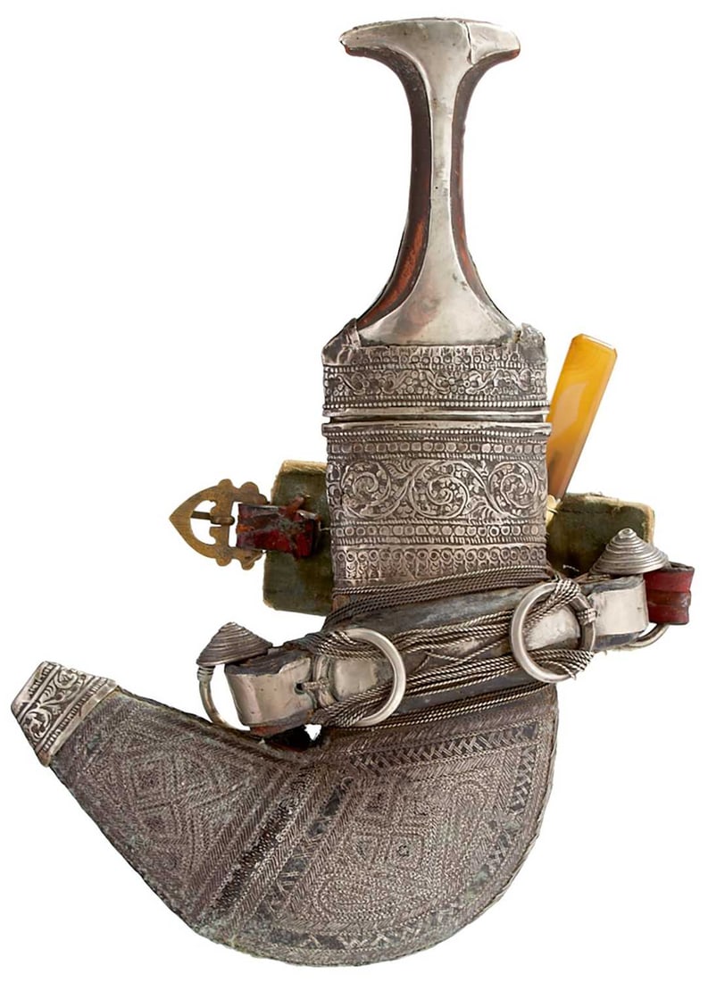 A MIDDLE EASTERN JAMBIYA OR DAGGER,: A MIDDLE EASTERN JAMBIYA OR DAGGER, 19cm sharply curved blade with raised medial ridge, white metal mounted horn hilt, in its white metal wrapped wooden scabbard, complete with hard stone hilted