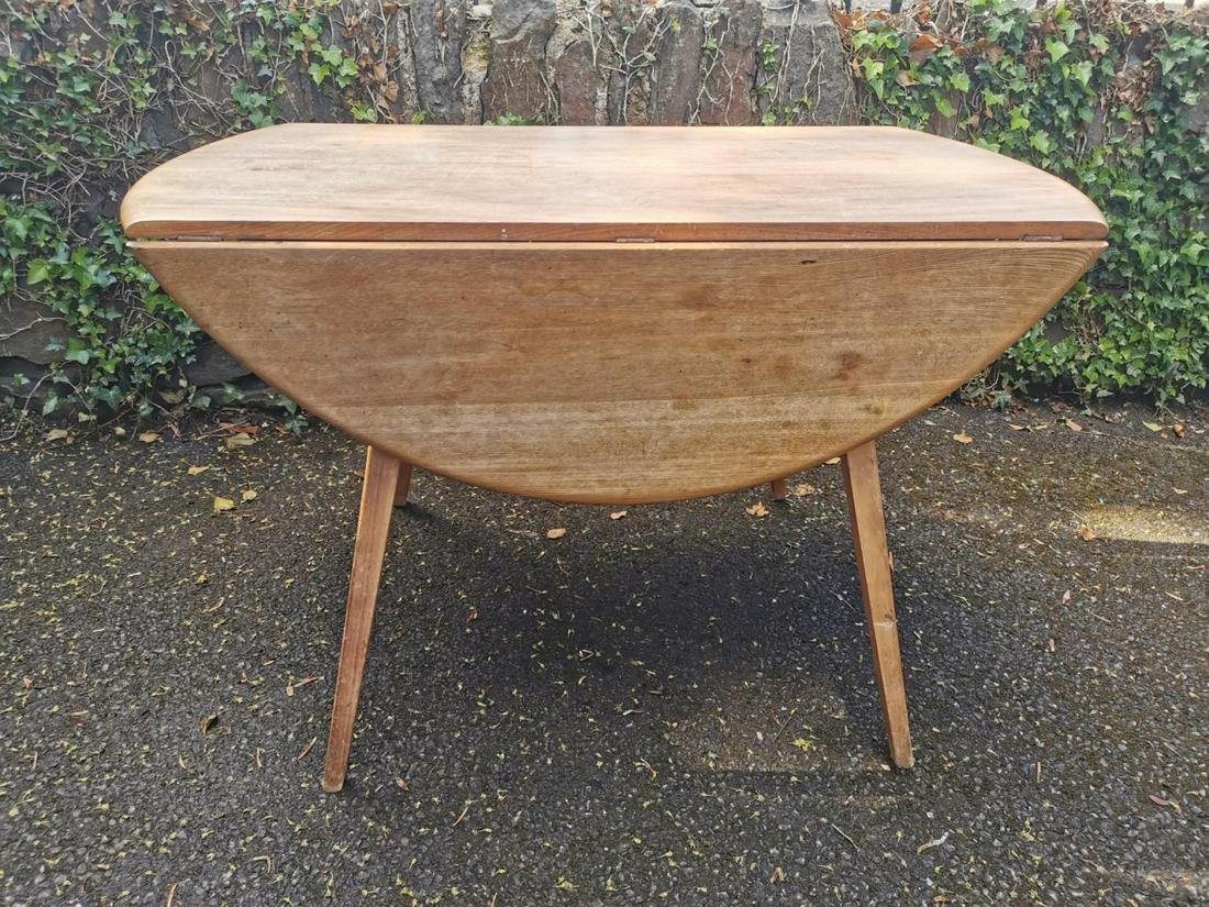 A light elm Ercol drop leaf table, of circular form on: A light elm Ercol drop leaf table, of circular form on four legs, with paper label, 71 cm high x 113 cm wide x 113 cm diameter (sides up)