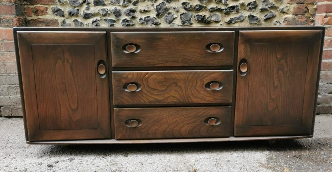 A dark elm Ercol sideboard, with three central drawers,: A dark elm Ercol sideboard, with three central drawers, one with cutlery drawer, flanked either side with a cupboard enclosing shelves, supported on shepherds castors, 68 cm high x 155 cm wide x 43 cm