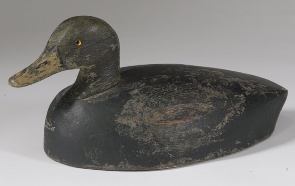 Joe Momney Black Duck Decoy, Wallaceburg ON: Intricately carved and hand painted wood with yellow inset glass eyes and signed on the bottom, 8"H x 17"W. There is wear throughout the decoy from age and normal use.