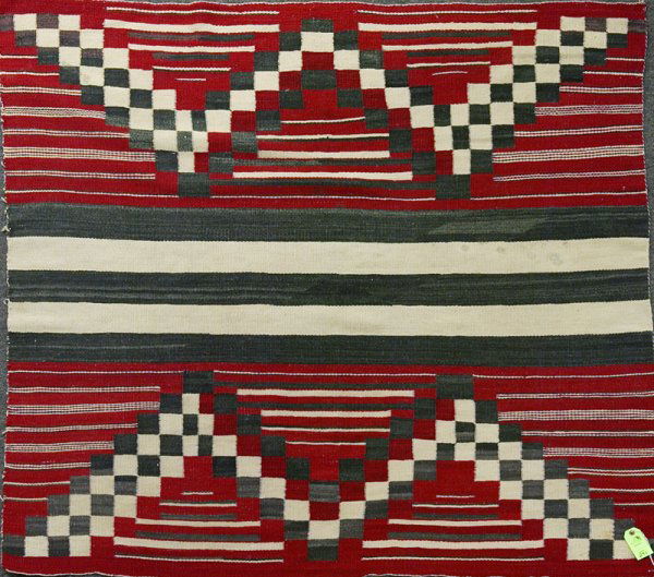 Navajo Rug: In a striped and checked pattern in red, navy and cream. Surface stains, with largest being a pink stain, and black dot stains which almost penetrate to other side. Fading and/or bleeding mainly to bl