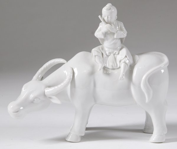 Chinese Blenc de Chine Water Buffalo and Child: A finely molded model of a standing water buffalo, with a child sitting on top playing a flute, with hat strapped to his back. 12" L x 9" H. Excellent condition.