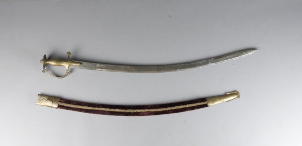 Curved Indian Sword with Brass Grip: Curved steel sword with brass grip and pommel, with burgundy velvet and brass scabbard. Made by Doon Steel Works Dehradun in India. Blade measures 31" L, some wear on blade and on scabbard. Circa 1960