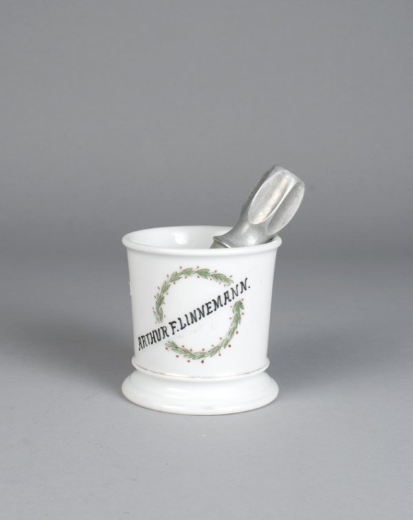 Antique Limoge Shaving Mug and Brush: Porcelain mug with the name Arthur F. Linnemann painted through a wreath. Together with a Rubberset brush. Mug measures 3.75" H, and has wear to gilt and paint. Private collection Metamora, Michigan.