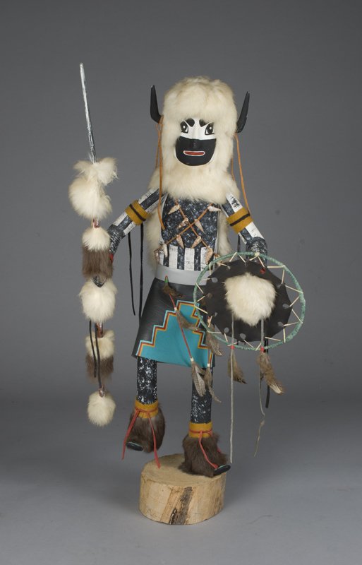 Very Large White Buffalo Kachina Doll: Solid wood painted in black and white with wood horns, fur headress, felt armbands, leather skirt, holding a fur lance in one hand and a fur and feather shield in the other. Fur boots and painted blac