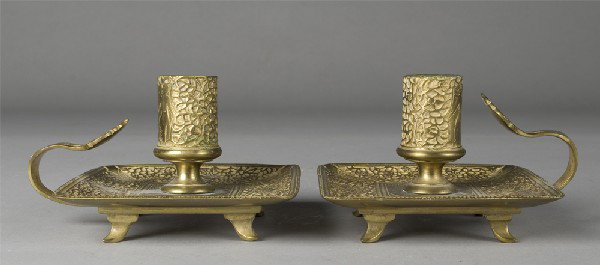 Pr. Of Handheld Brass Candlesticks: Each plate decorated with four areas of a figure on a horse amid scrolling designs. Candle holder decorated with standing figure amid scrolling designs. Both rest on four feet. 3.5" H x 4 & 5/8" Sq.