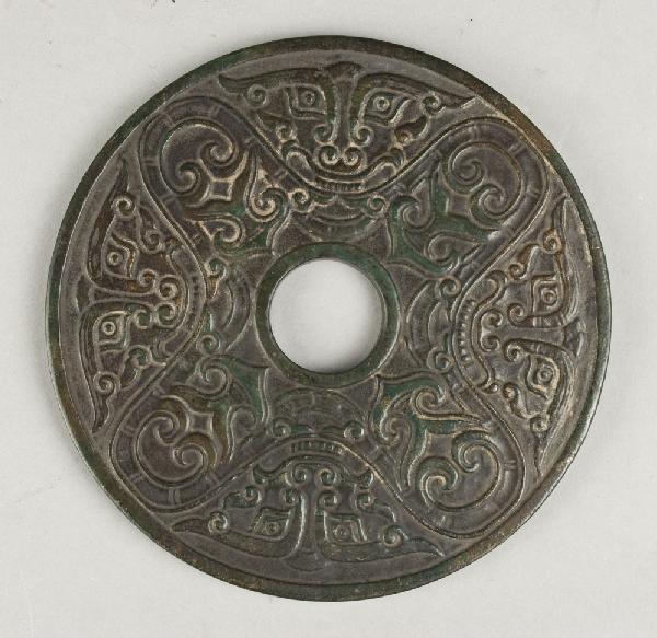 A Large And Fine Chinese Carved Jade Bi Disc: Finley carved on both sides to depict the face of the beast and alternating archaic symbols, possibly Han dynasty, the jade a spinach green with some natural russet inclusions. 4.75"diameter.