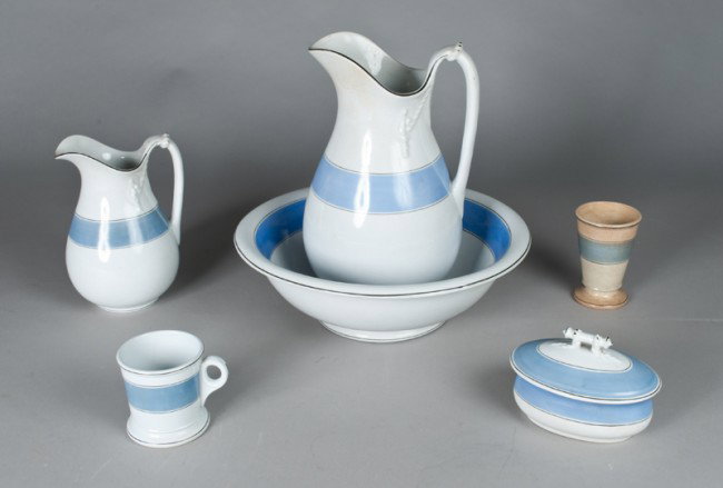 Antique N.J. Pottery Company Wash Set: In blue and white, includes large pitcher, basin, small pitcher, covered soap dish, and shaving mug. Also included drinking cup unmarked. Tallest 13" H. All with crazing and minor staining and drinkin
