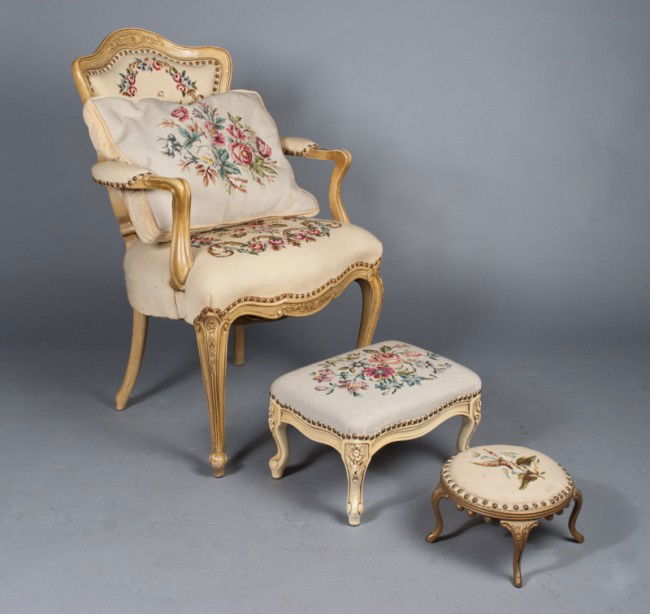 French Needlepoint Chair and Two Ottomans: French arm chair in antiqued white, with needlepoint seat and back, with two footstools one with iron base, both with needlepoint covers 36"H x 26"D x 23"W, circa 1940's.