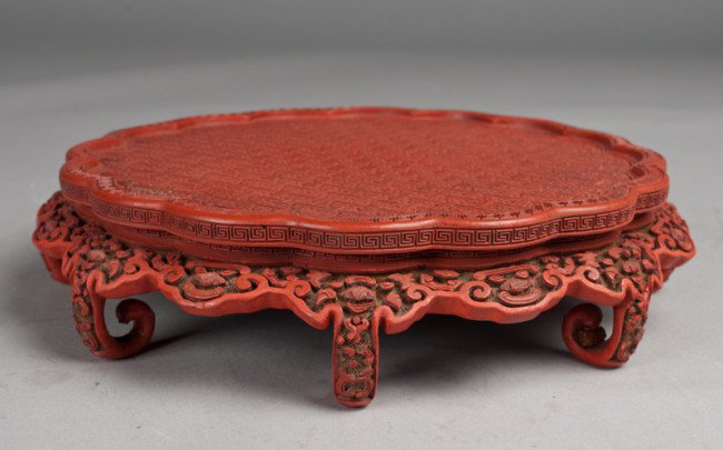A Fine Chinese Cinnabar Stand: Finely carved to depict lucky symbols with scalloped top, and eight pearled legs, 9.25"D X 2"H, loss to one leg at the end, a very nice stand.