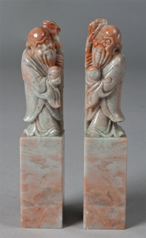 Pr. Of Fine Chinese Soapstone Chops: Each finely carved to depict elders holding a ruyi sceptre and peach. The stone a medium lavender with burnt orange inclusions, particularly on the face. Definitely done by a skilled carver. 4.875" H,
