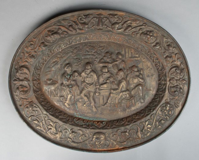 Antique Cast Iron Figural Wall Plaque: Oval plaque depicting figures in a tavern scene with outer rim decorated with floral, scroll and grotesque mask design. 16" H x 20.5" W, rust and oxidization throughout. Late 19th/early 20th century.