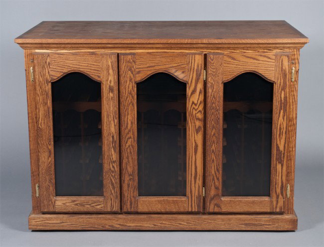 A Fine Oak And Glass 168 Bottle Wine Cellar: Three door credenza oak wine cellar with crowned top, able to hold 168 bottles, from United Cellars. 37" H x 52" W x 29" D. Minor wear to surface from use, may need refrigerant. Original paperwork inc