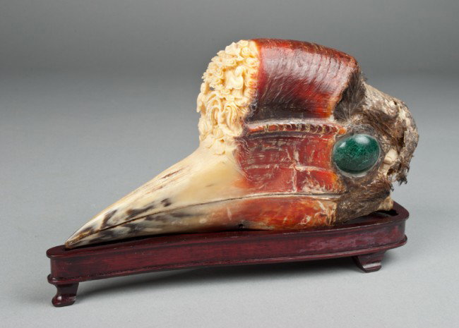 A Fine Chinese Carved Hornbill Casque: The top portion carved with a scene of two figures in an idealic landscape, presented on a fitted wood stand. 8" L x 4.25" H, circa late 19th/early 20th century.