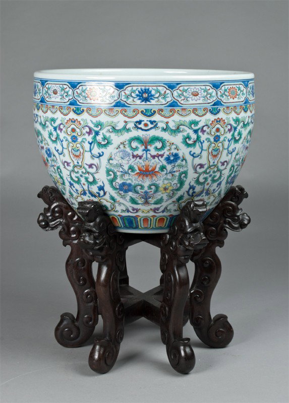 A Fine Chinese Famille Rose Bowl On Zitan Stand: Finley enameled to depict circular medallions of flowering lotus amongst lotus tendrils, the base marked for great Qianlong production, displayed on a carved zitan wood stand with dragon terminals, 9"