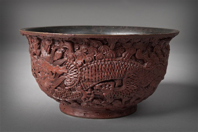 Chinese Qing Carved Cinnabar Footed Bowl: Finley carved to depict dragons chasing a flaming pearl, the footed base with sic character mark in gilt for Great Qing Qianlong Production, 6.5"D x 3.375"H, circa 19th century.