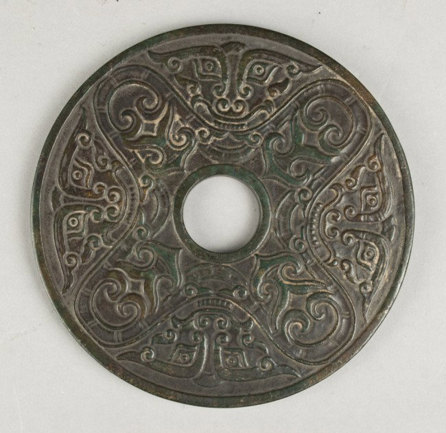 A Large And Fine Chinese Carved Jade Bi Disc: Finley carved on both sides to depict the face of the beast and alternating archaic symbols, possibly Han dynasty, the jade a spinach green with some natural russet inclusions. 4.75"diameter.